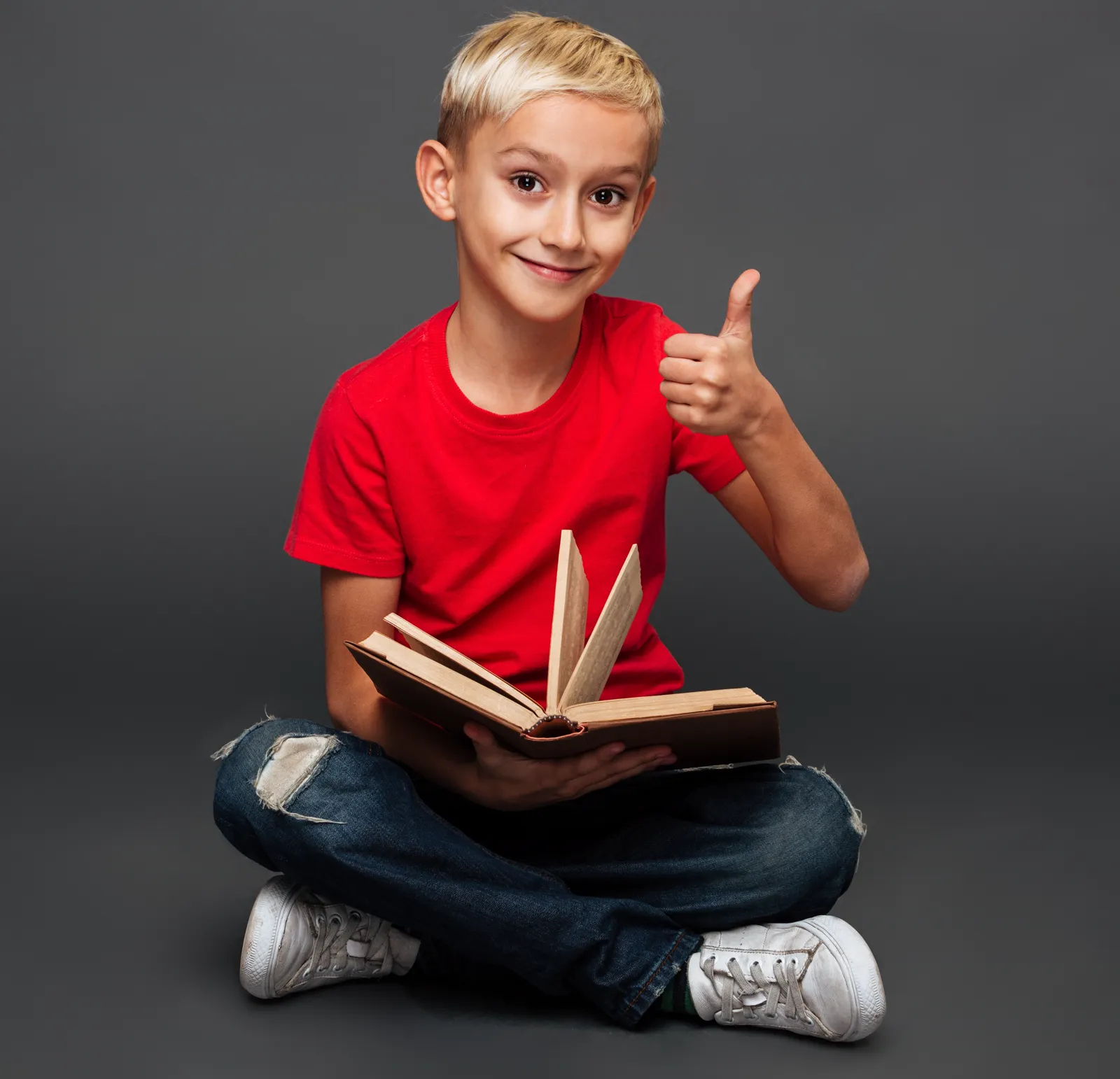 Smiling boy holding an open book and giving a thumbs up