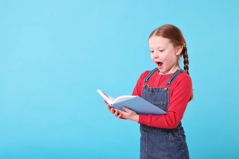 Girl reading a book, wide eyed with excitement