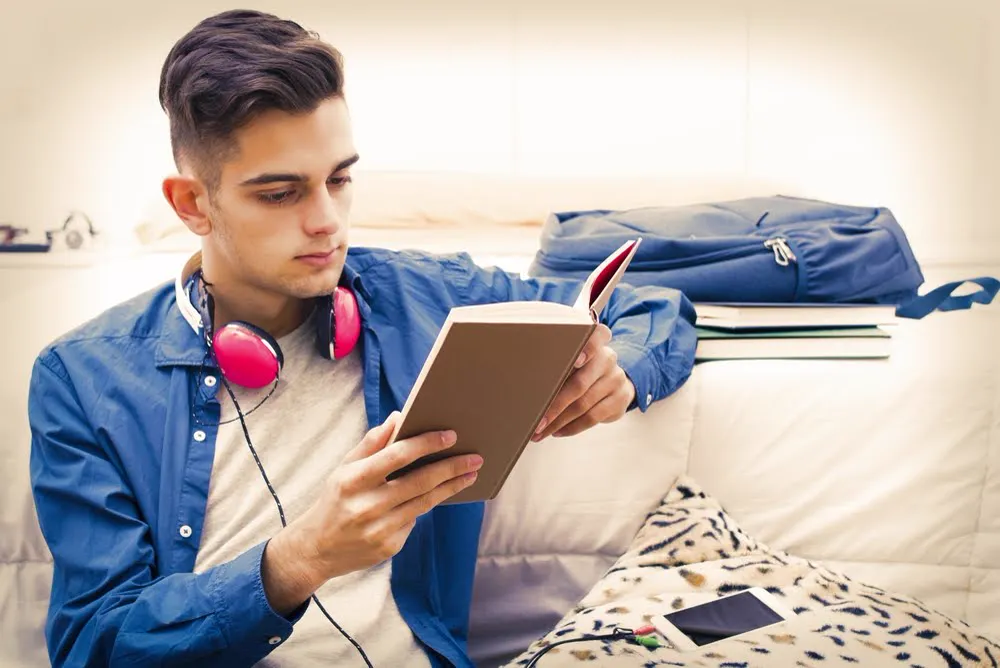 Teenage boy with headphones around his neck reading a book